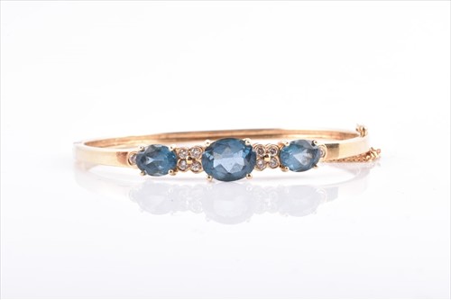 Lot 600A - A yellow metal, diamond, and blue topaz bangle...