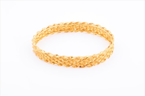 Lot 418 - A yellow metal bangle bracelet of textured...