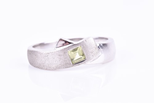 Lot 791 - A white metal and peridot crossover ring, the...