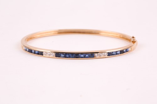 Lot 219 - A yellow metal, diamond, and sapphire bangle,...