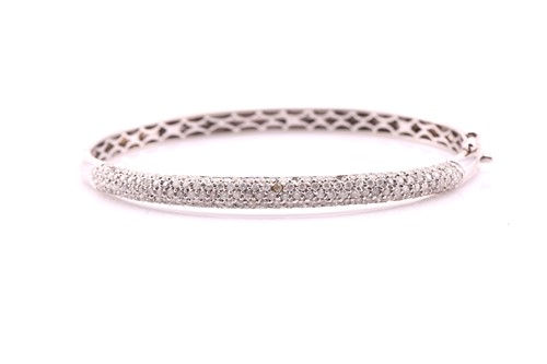 Lot 246 - 18ct white gold hinged bangle, one side pave...