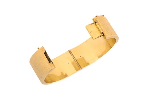 Lot 145 - A textured yellow metal hinged bangle, the...