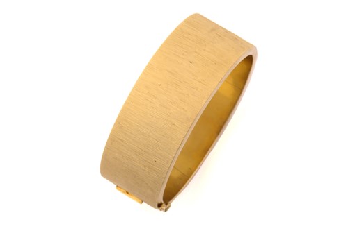Lot 145 - A textured yellow metal hinged bangle, the...