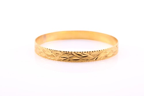 Lot 412 - A yellow metal bangle, with stylised leaves on...