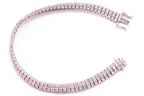 Lot 19 - A three-row diamond tennis bracelet, featuring...