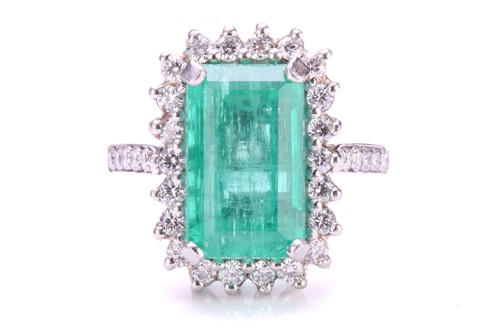 Lot 299 - An emerald and diamond halo ring in platinum,...