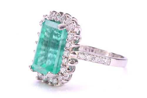 Lot 299 - An emerald and diamond halo ring in platinum,...