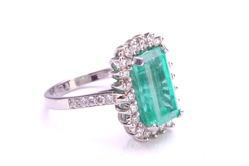 Lot 299 - An emerald and diamond halo ring in platinum,...