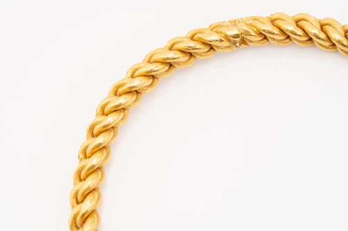 Lot 140 - A high-carat gold closed bangle, of braided...