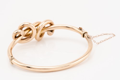 Lot 221 - A rose gold knot bangle; the hinged hollow...