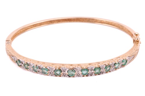 Lot 102 - An emerald and diamond bangle, set with a row...