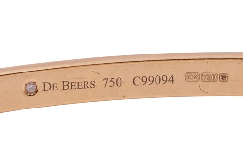 Lot 56 - De Beers - a hinged bangle in 18ct yellow gold,...