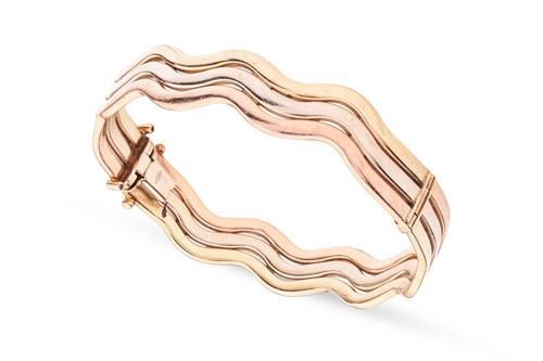 Lot 154 - A three-tone wavy hinged bangle, the bracelet...